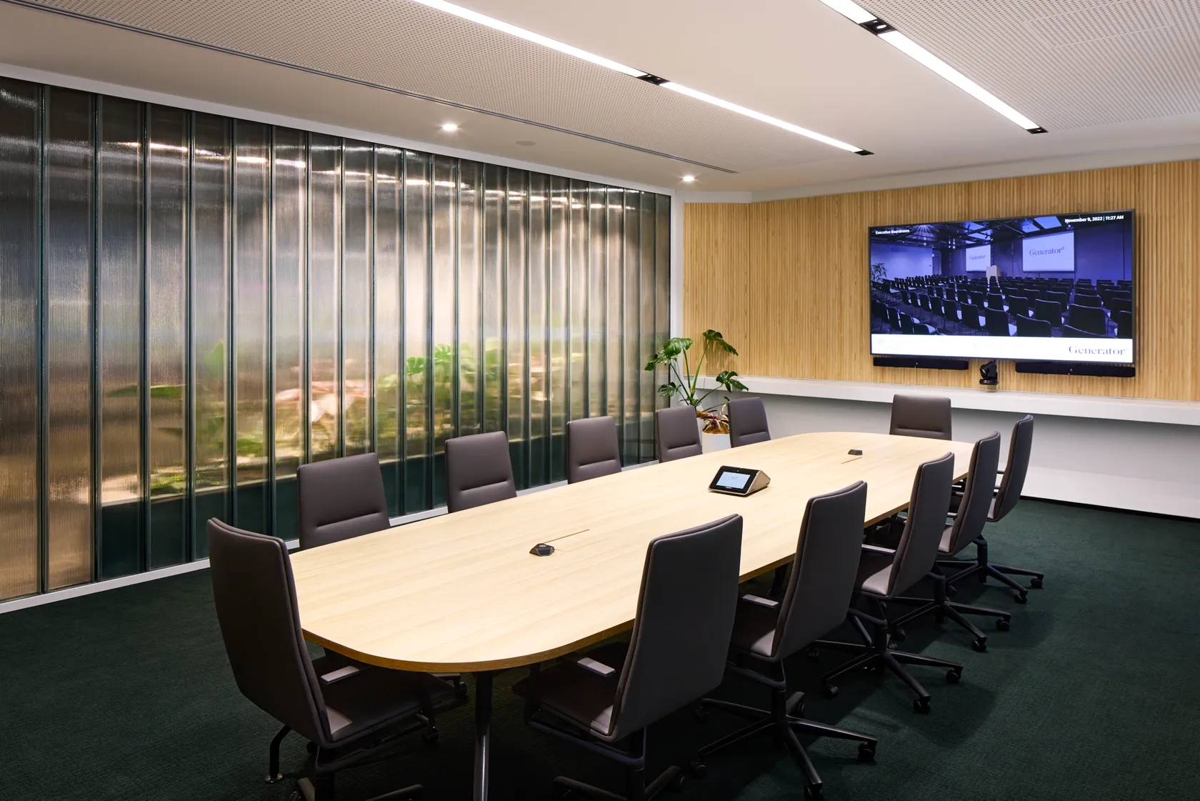 Boardroom with oval timber table, leather chairs, timber louvre wall feature, large screen, and green carpet