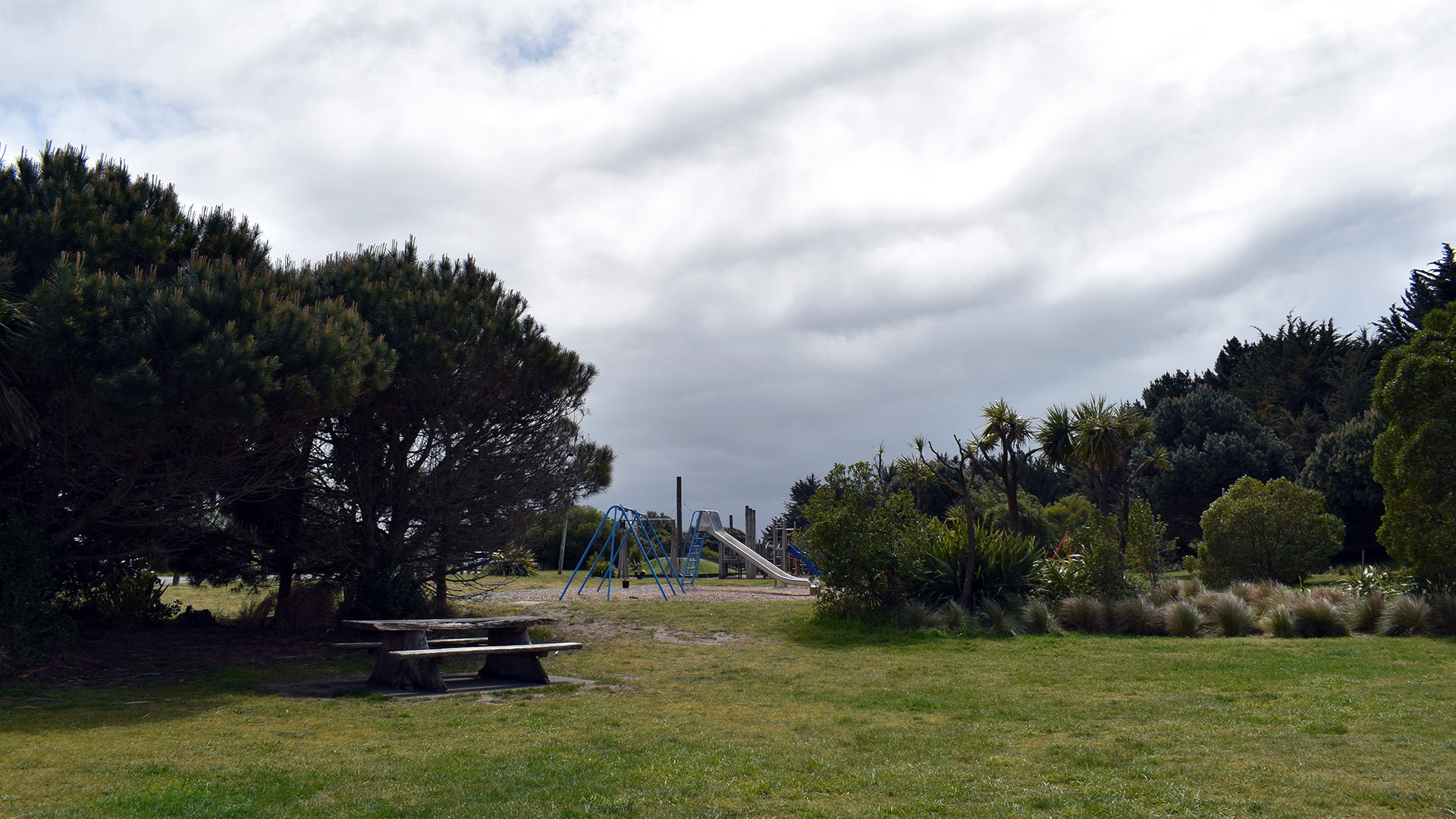 Grassed park area with trees and playground equipment in background