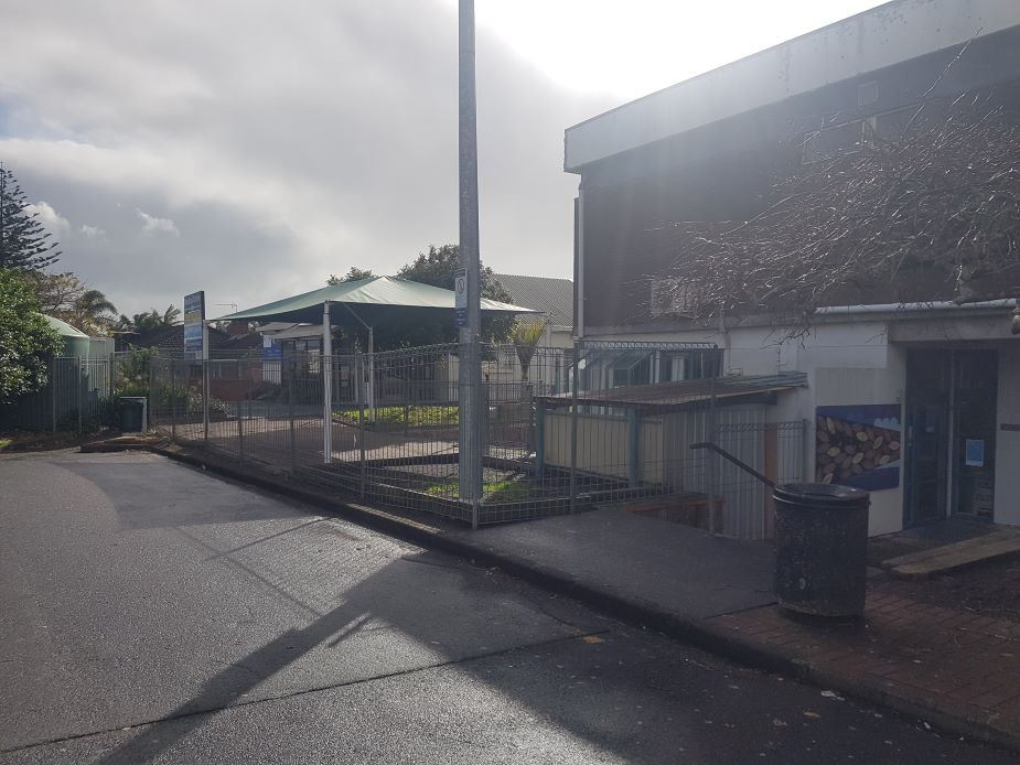Street-side view of building entrance with fenced outdoor area and shade sail