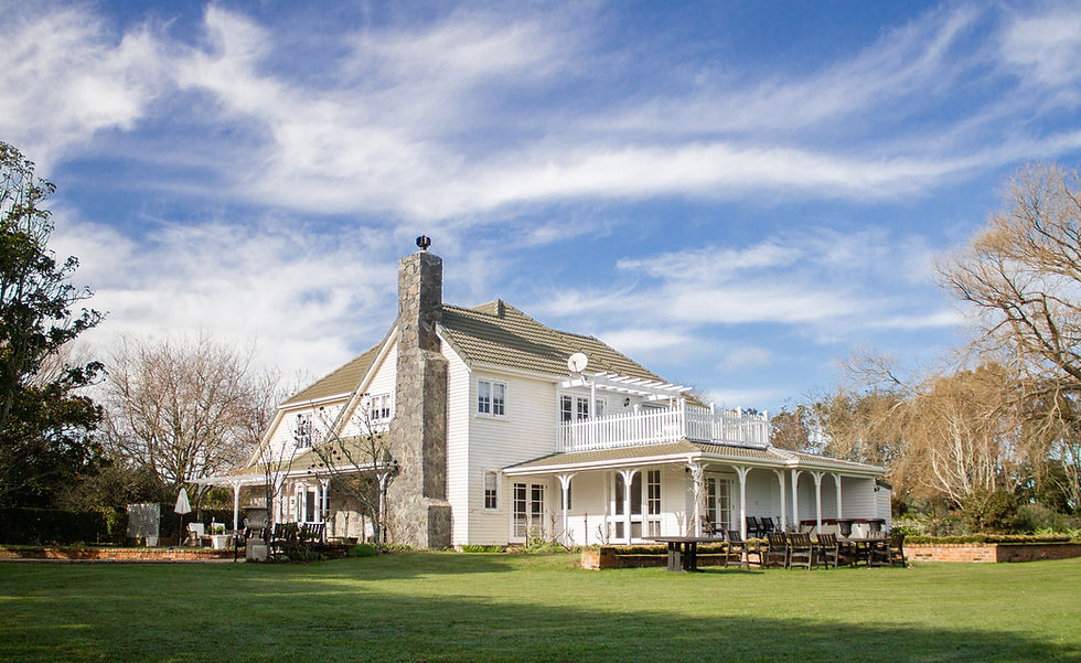 Two-storey white country homestead with verandah and stone chimney set in open lawn