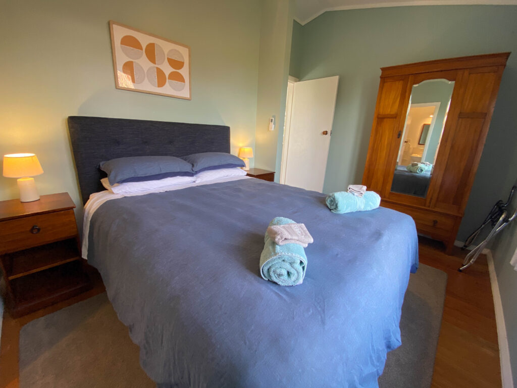 Blue-grey bedroom with a double bed, timber bedside tables, wooden wardrobe, and wall art