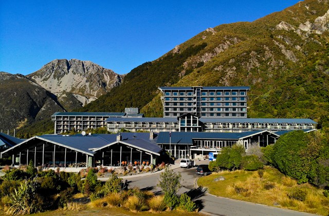 Multi-storey hotel complex with low-pitched roofs set against steep bush-covered mountain slopes