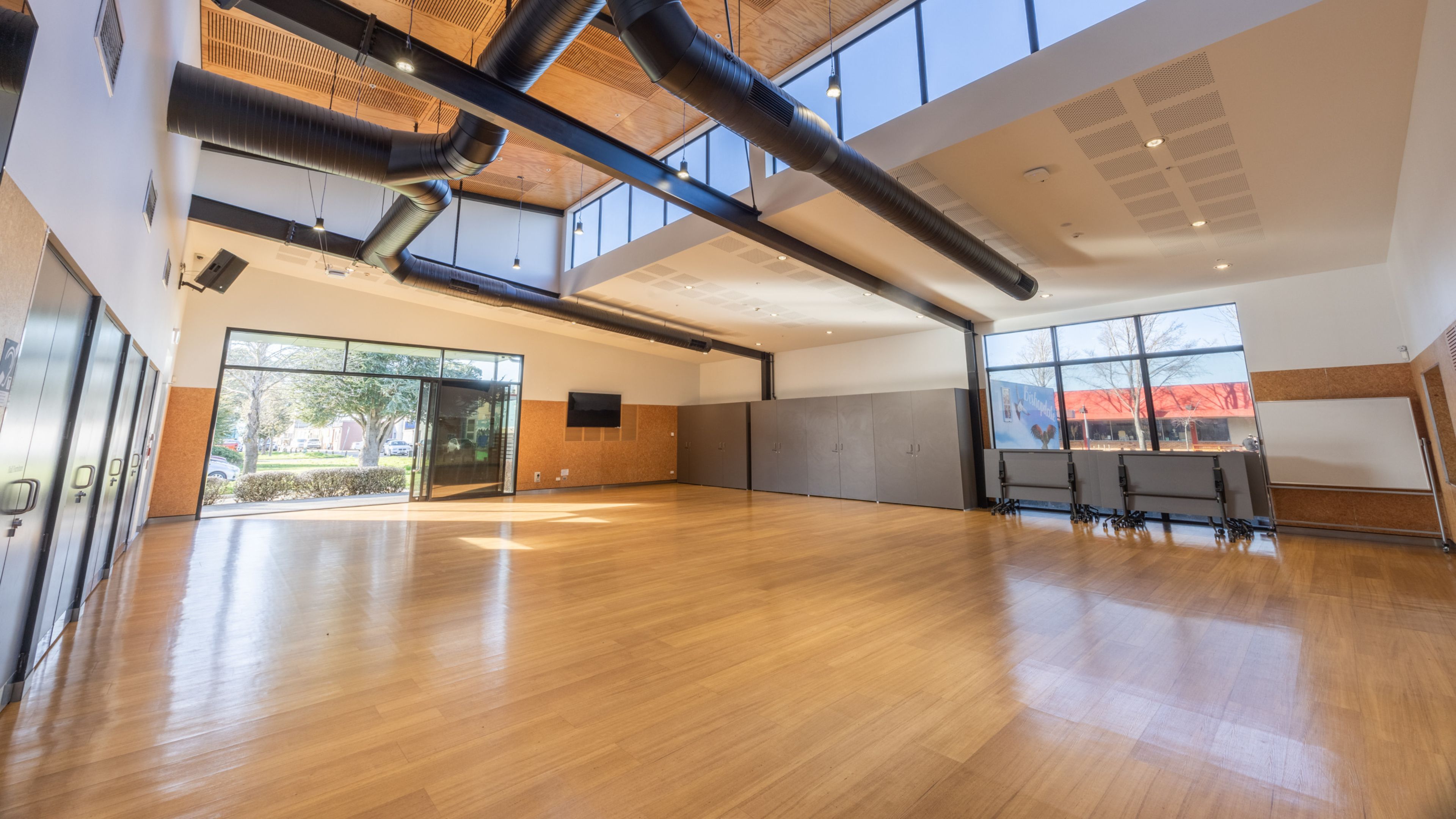 Large open hall with timber floor, exposed duct services, and coloured glazed panels