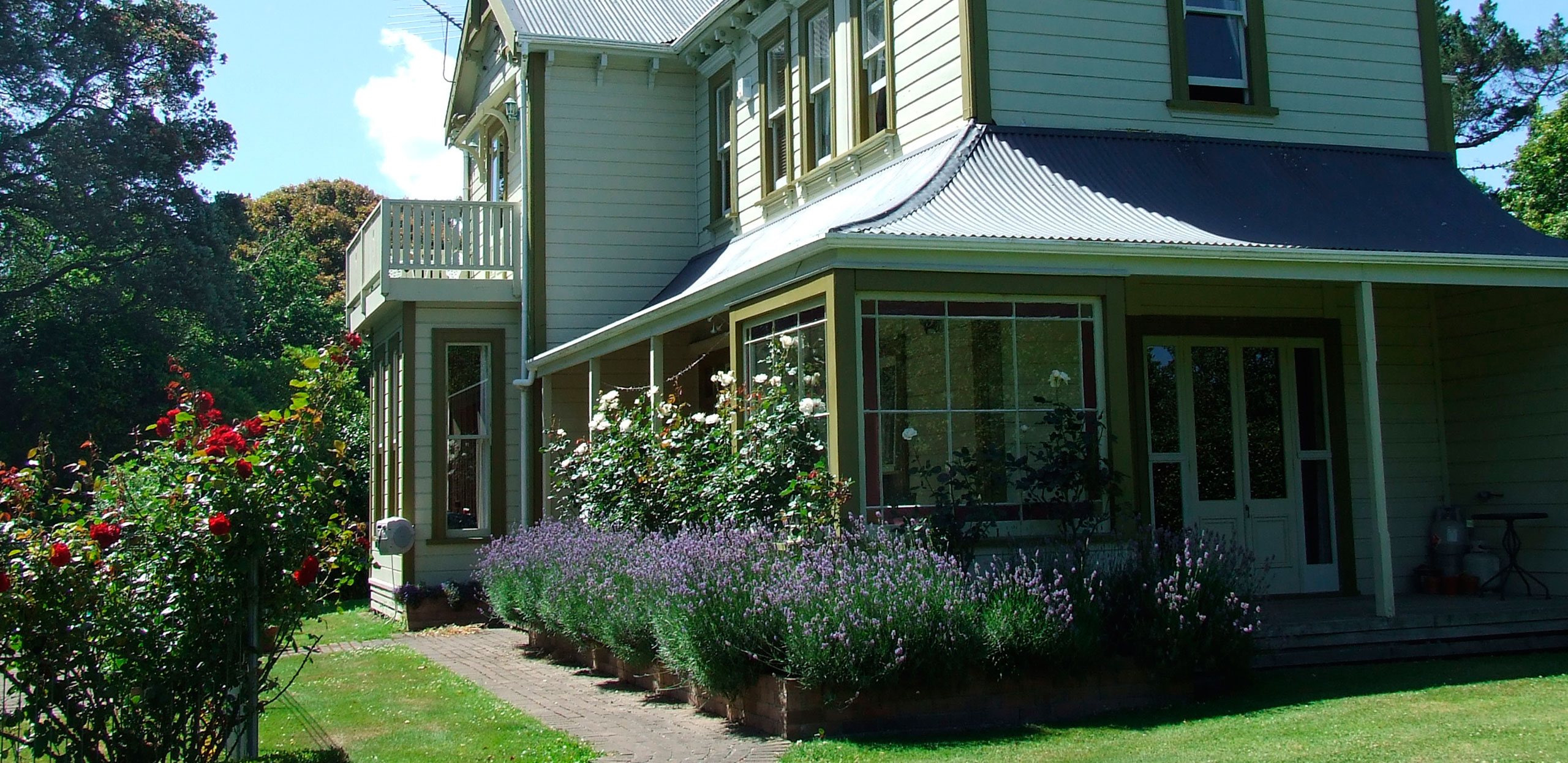 Two-storey villa exterior with a verandah, lavender garden border and mature trees