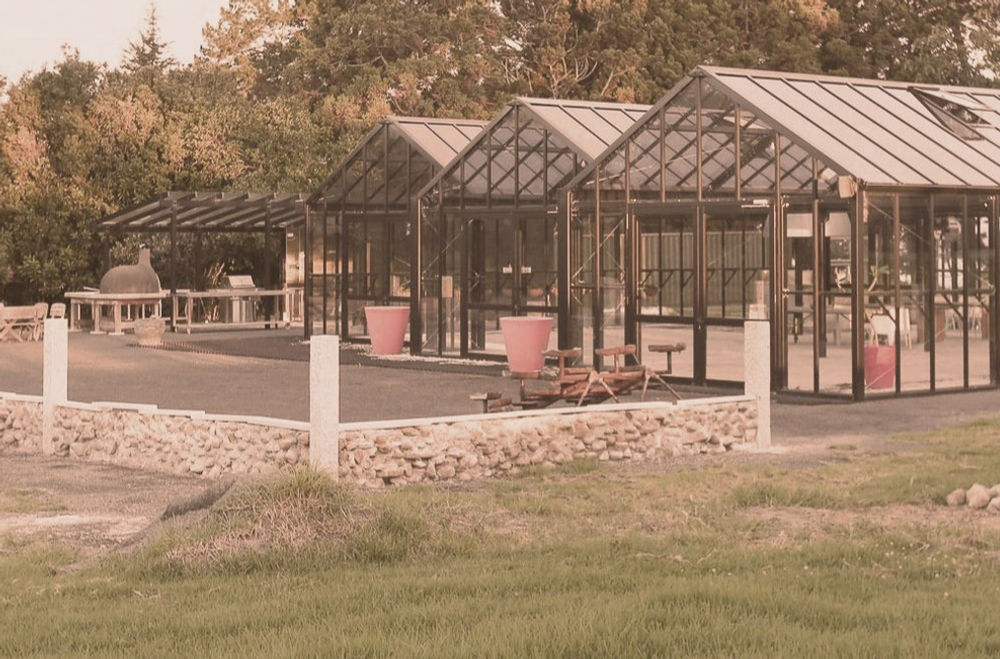 Black steel-framed glasshouse structures with stone wall surround, open rural setting