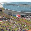 Large arena building with crowd on surrounding lawn at outdoor event