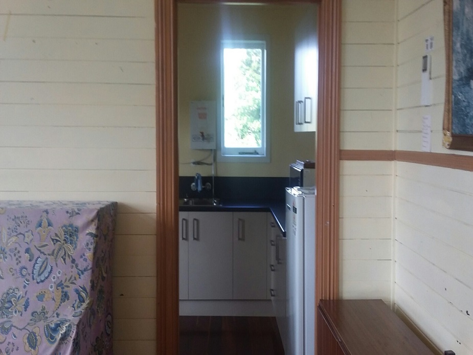 Small hall room with kitchenette visible through doorway and timber walls