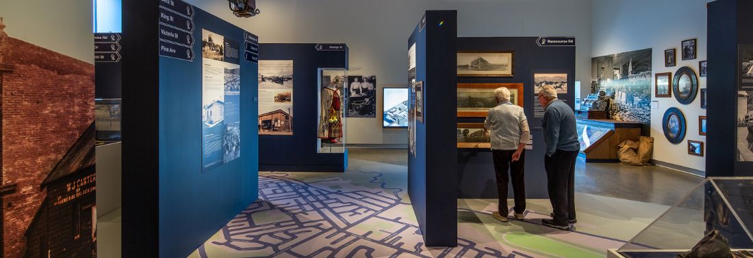 Museum exhibition hall with blue display panels, photographs, and map floor