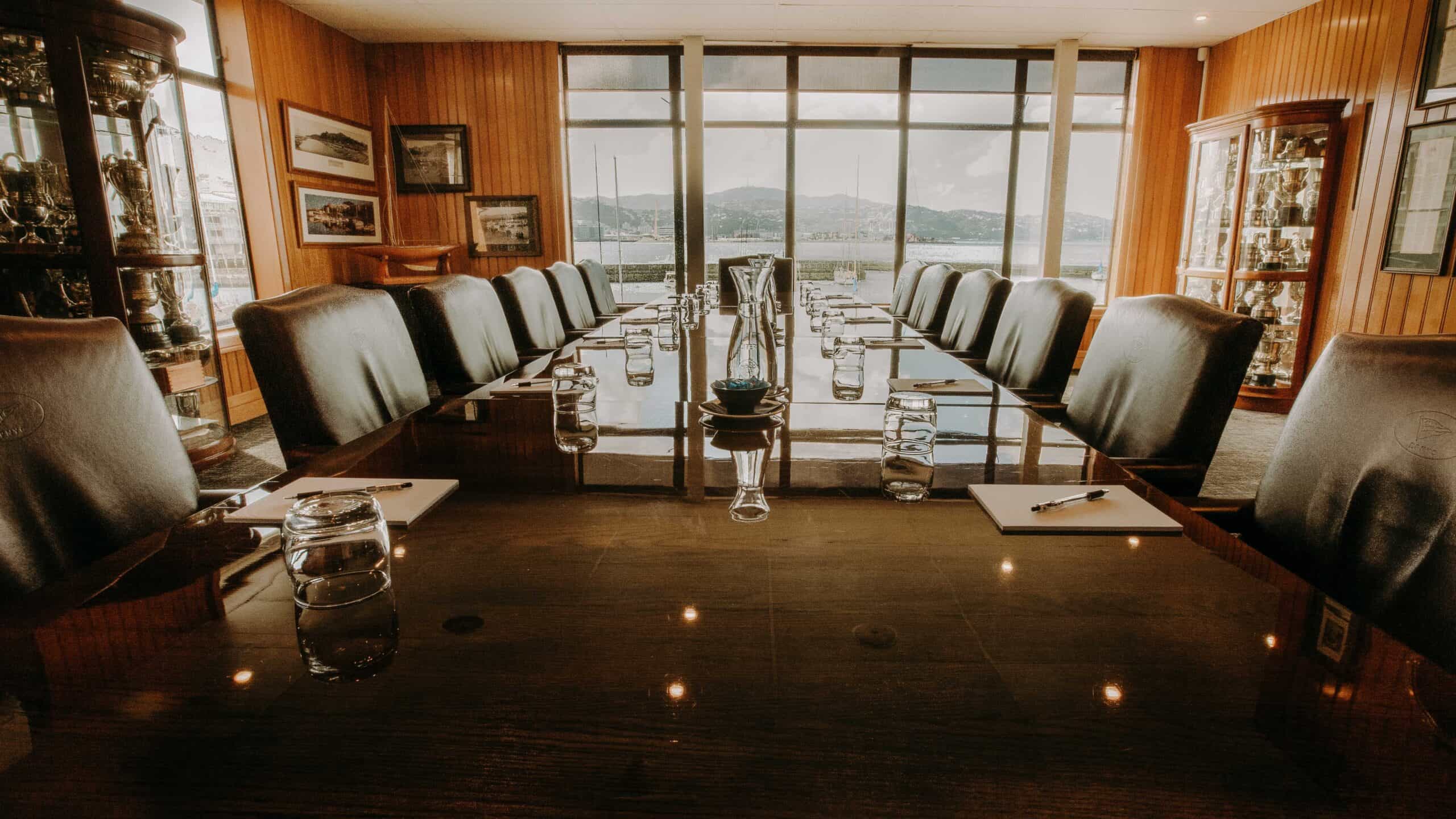 Polished timber boardroom with dark leather chairs, large windows framing a harbour view