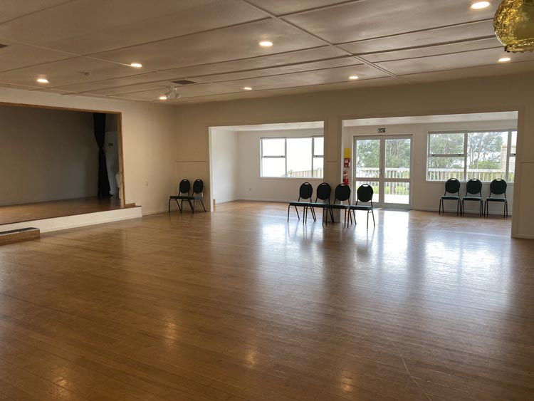 Empty community hall with timber floor, raised platform and windows