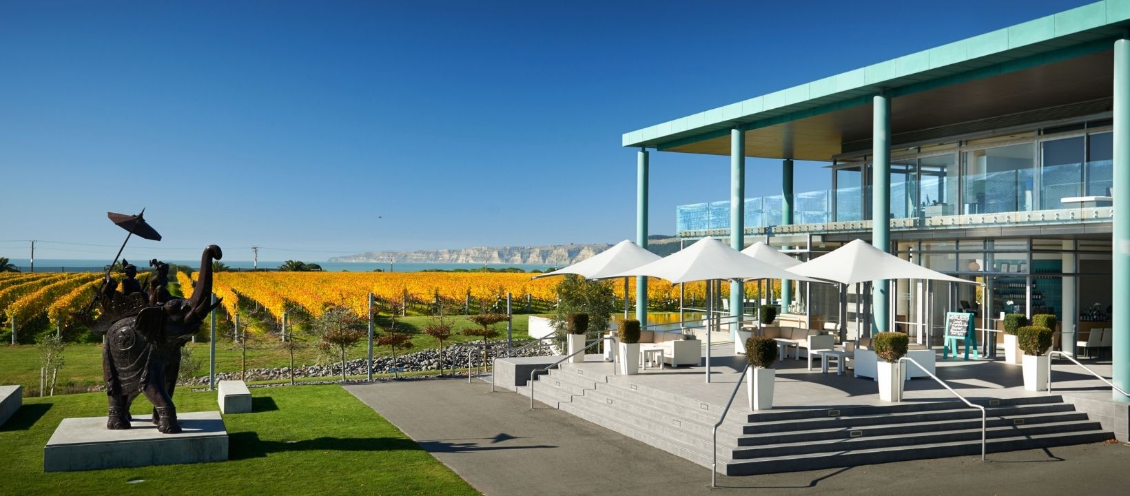 Winery exterior with an elephant sculpture, autumn vineyard rows and coastal cliffs beyond