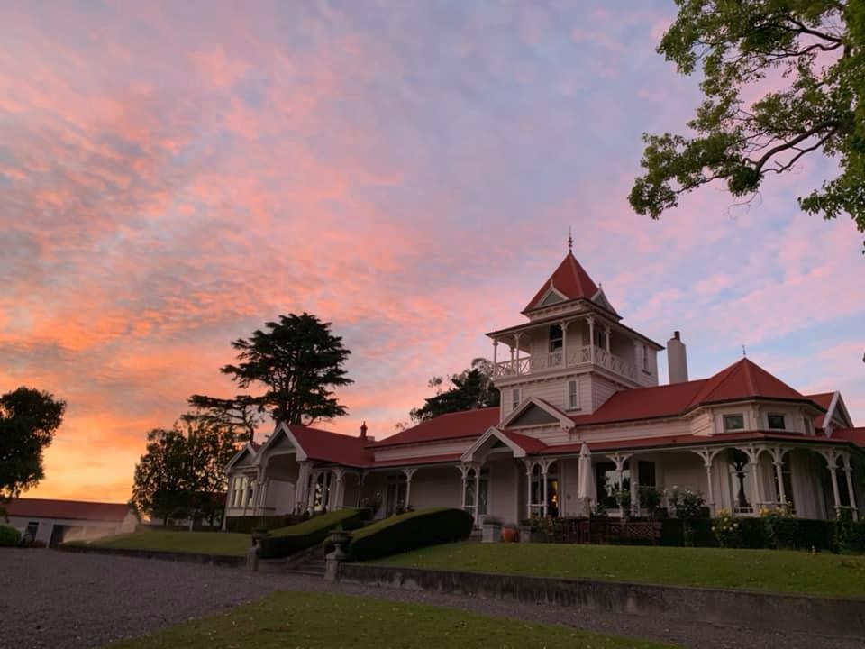 Victorian-era homestead with red-tiled roof and wraparound veranda at sunset