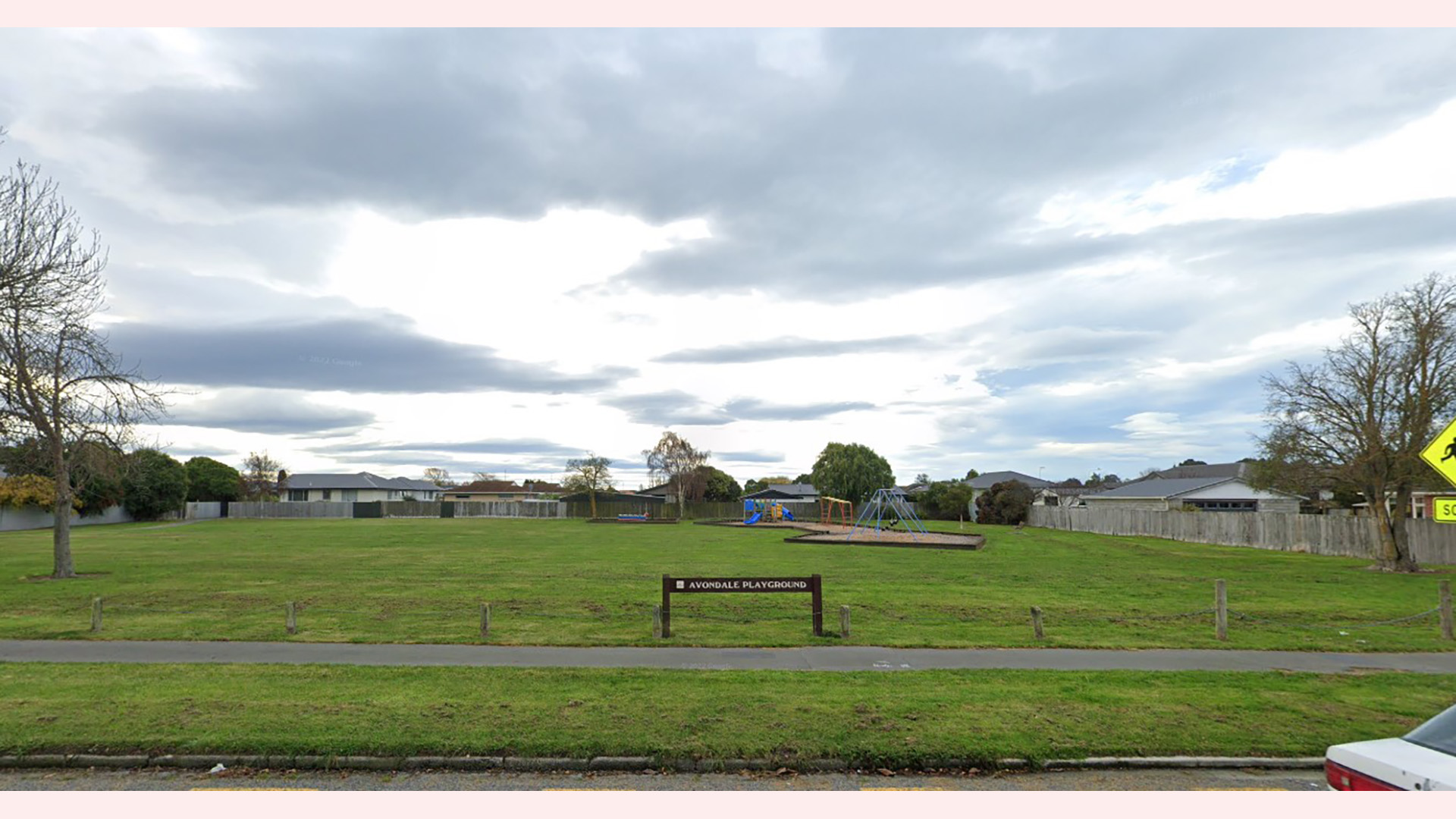 Open grass reserve with a playground area and signage near a residential street