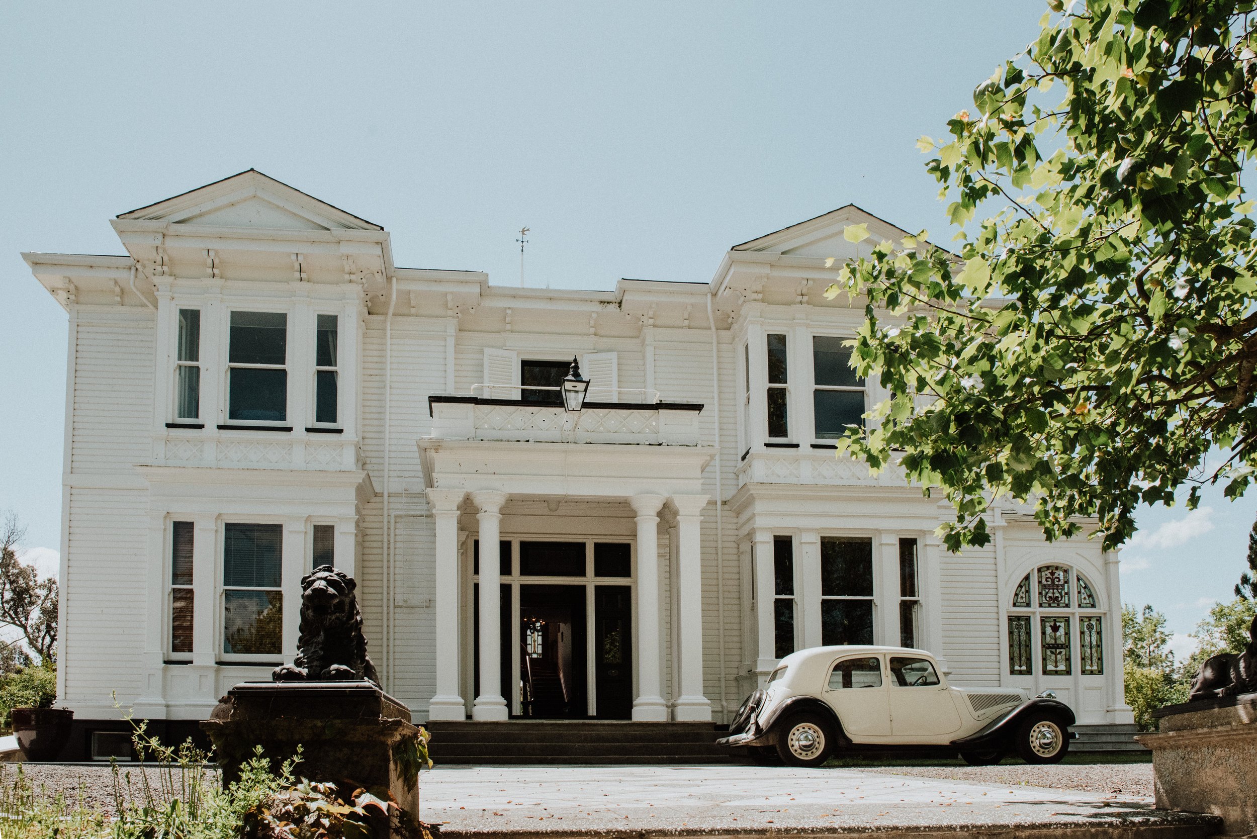 White two-storey villa facade with vintage car parked at entrance