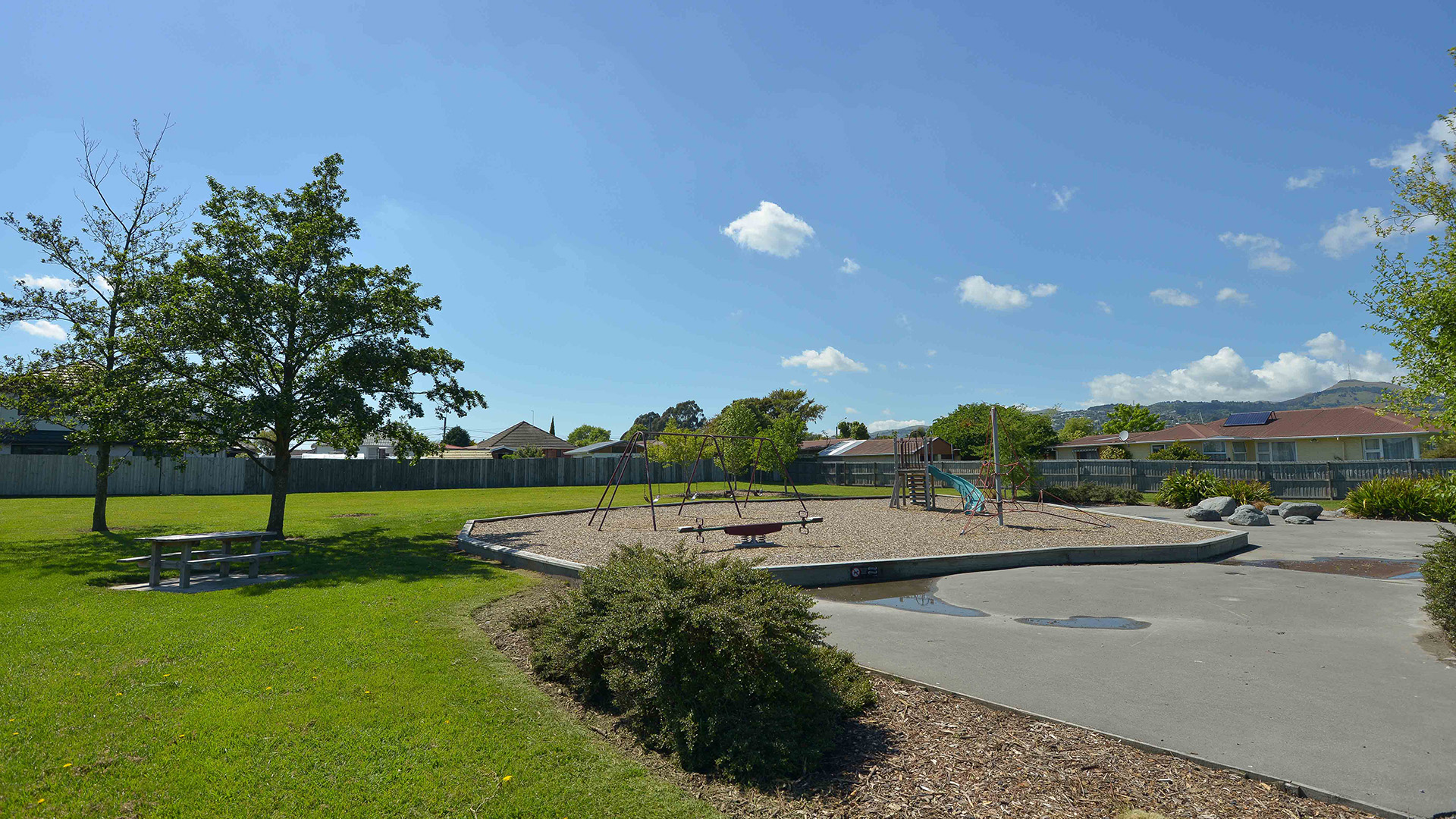 Open grassed reserve with playground equipment, picnic table and trees
