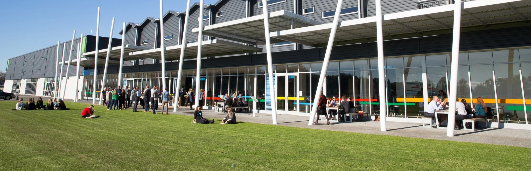 Modern events centre exterior with white colonnade and lawn area with attendees