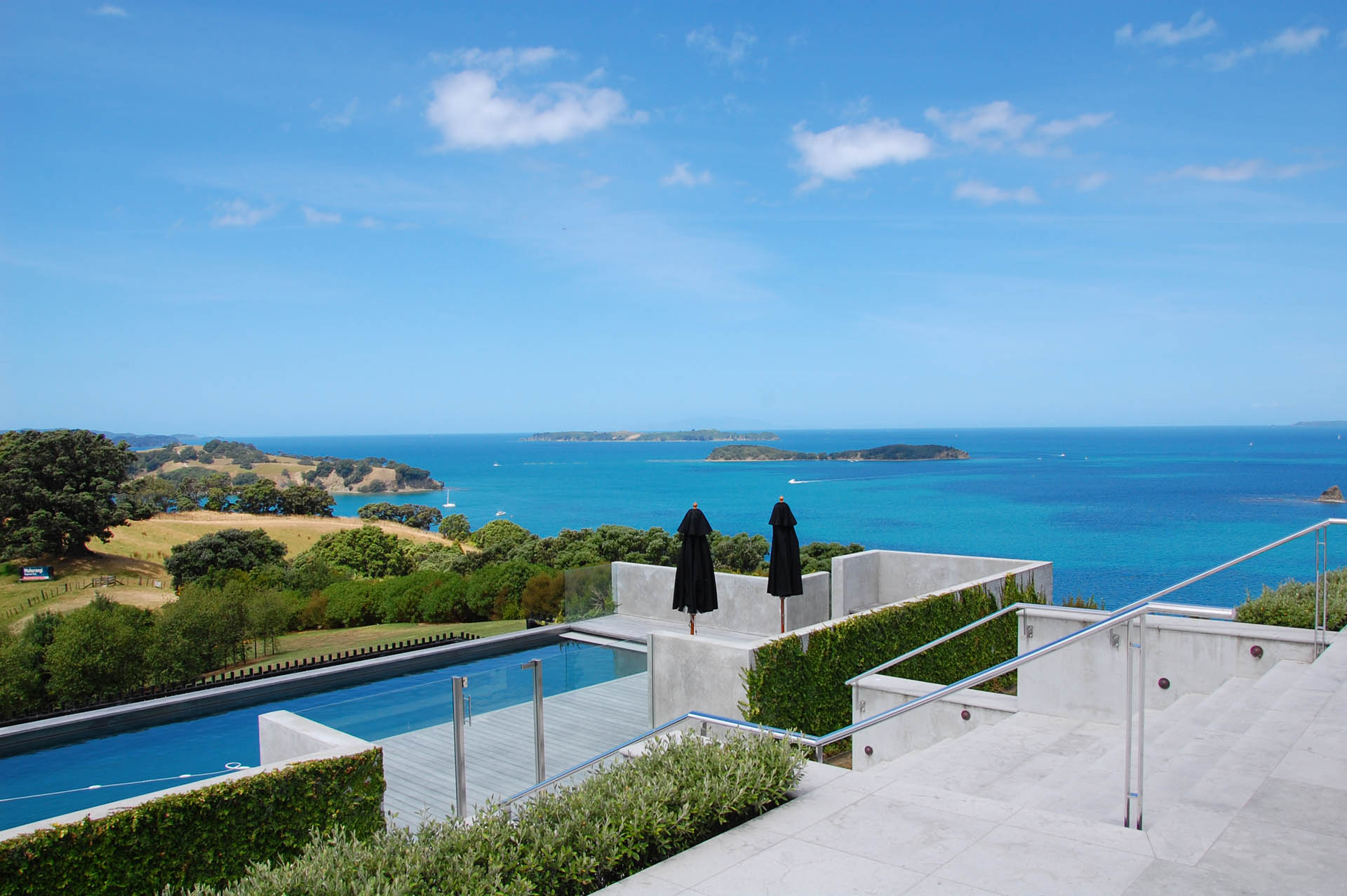 Elevated infinity pool deck with sun loungers overlooking blue bay and green hills