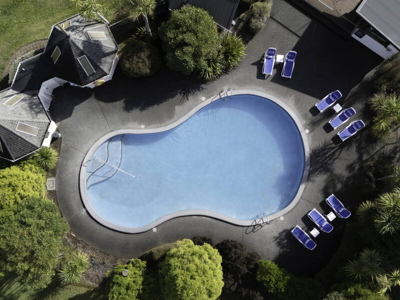 Aerial view of curved outdoor pool with sun loungers and surrounding gardens