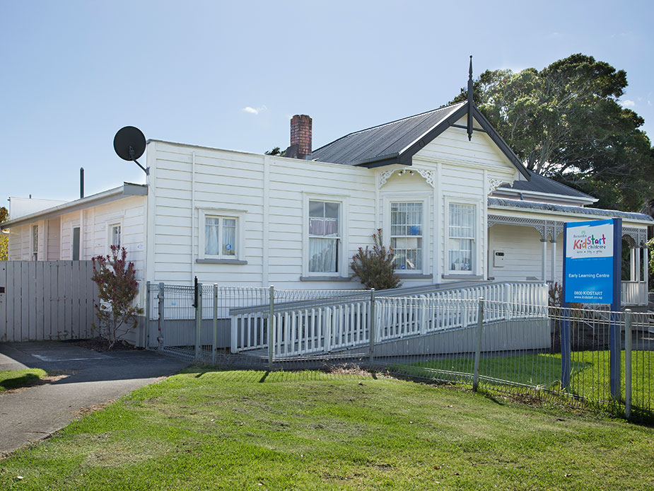 White timber villa exterior with pitched roof and decorative gable, white picket fence, green lawn