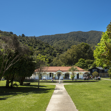 White homestead building on lawn with hills and trees behind
