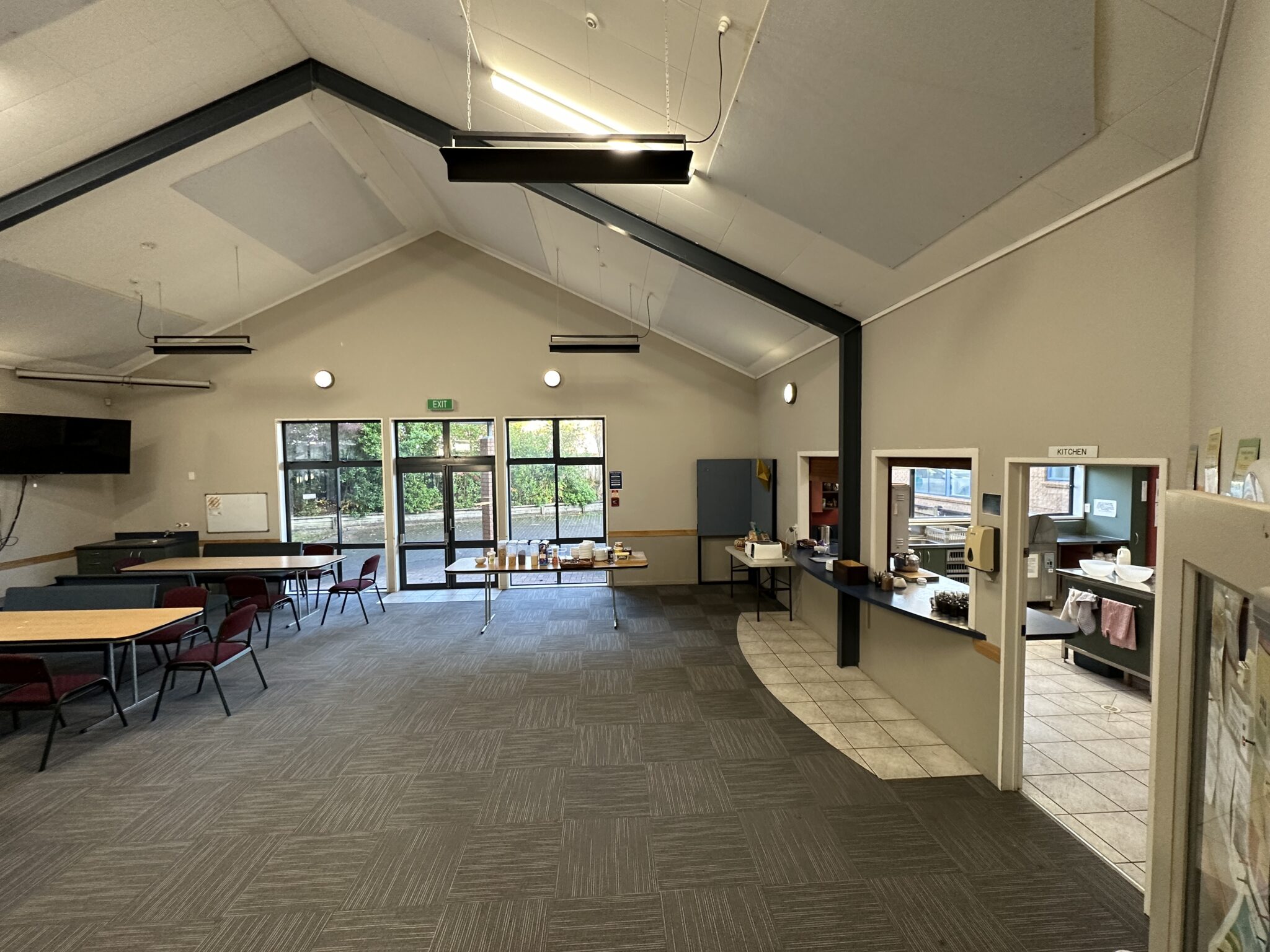 Vaulted community hall with tables, chairs and pass-through kitchen window