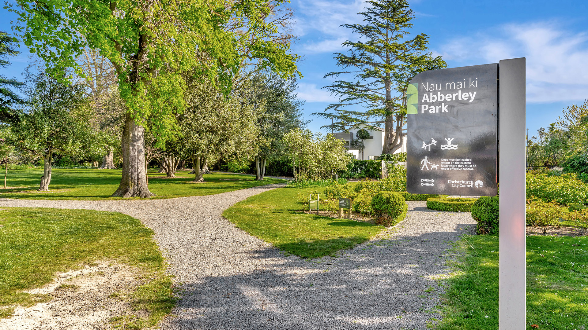 Park entrance with gravel path, park signage, and lawns