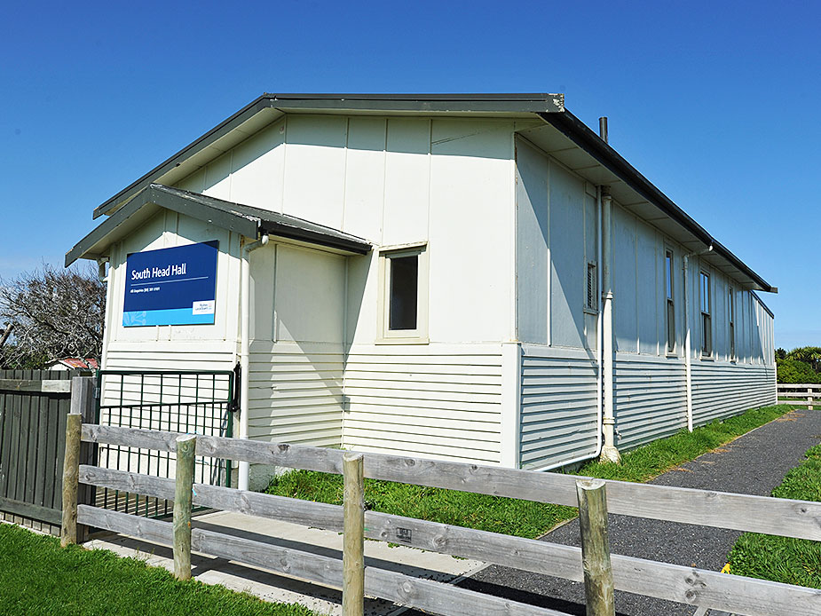 White-painted corrugated metal hall with a low-pitched roof and signage beside a path