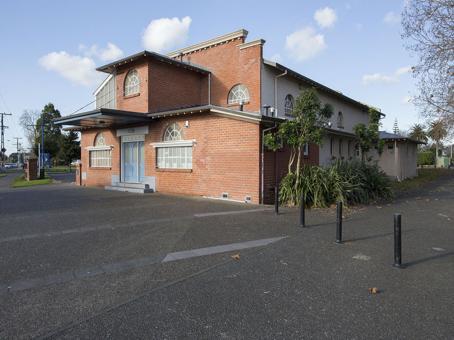 Red-brick two-storey community hall exterior with arched windows, car park and street frontage
