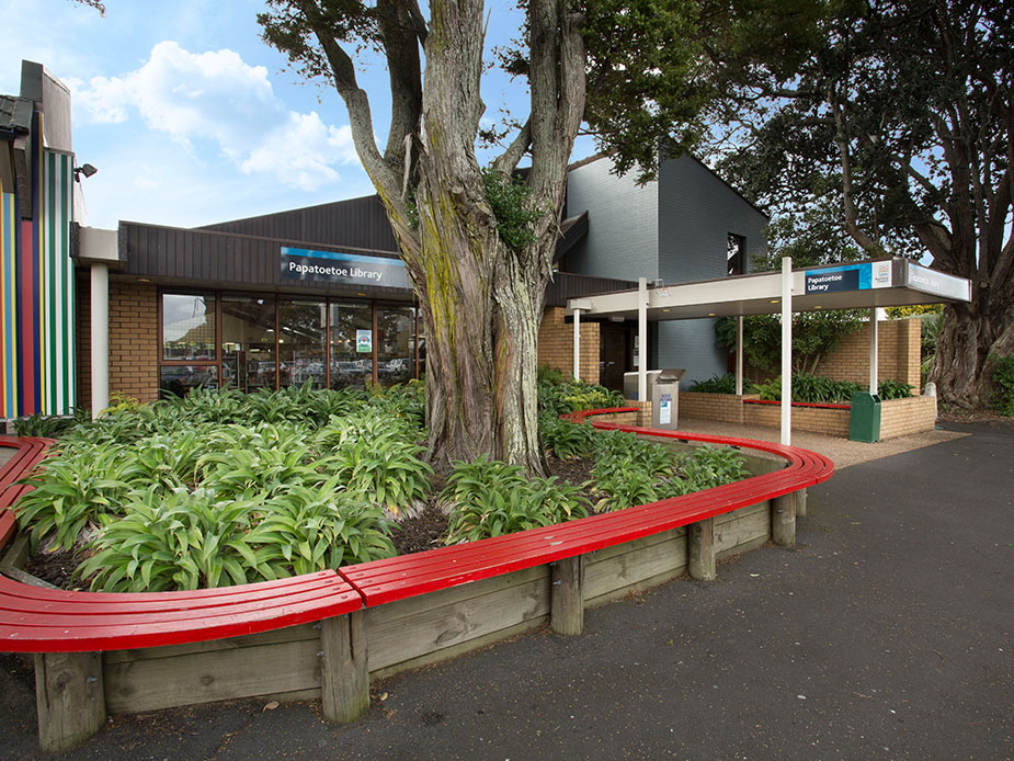 Library building exterior with large tree, curved bench seating and planting