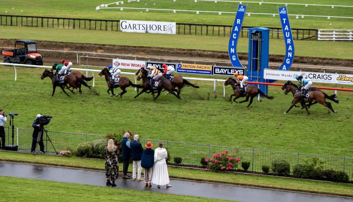 Horse race in progress on turf track with spectators watching from trackside