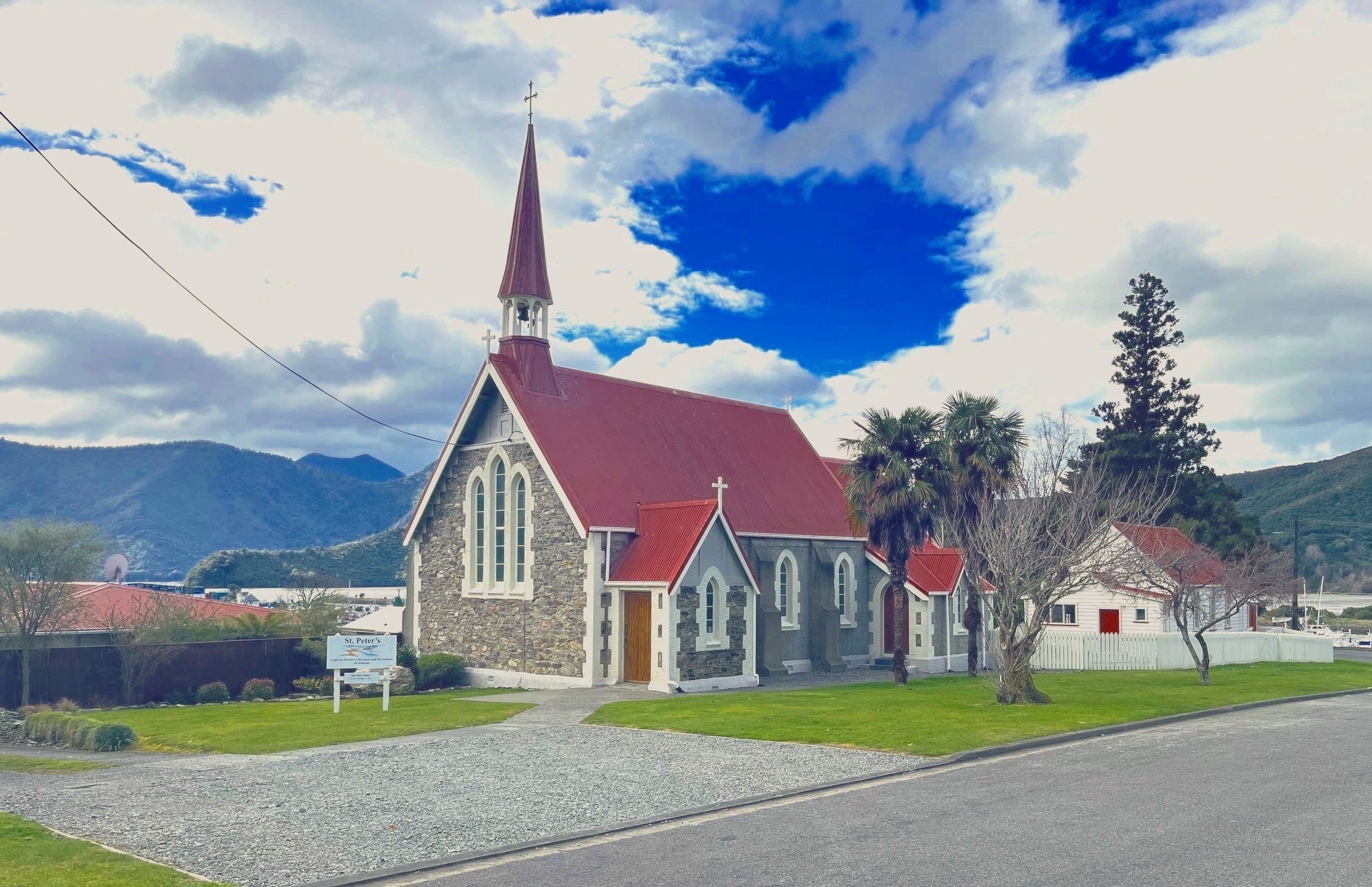 Stone church with red corrugated roof and steeple against blue sky