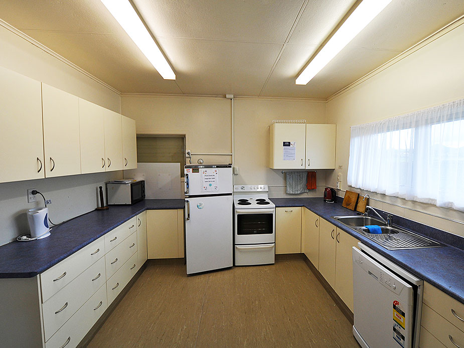 Hall kitchen with cream cabinets, oven, refrigerator and dark bench tops