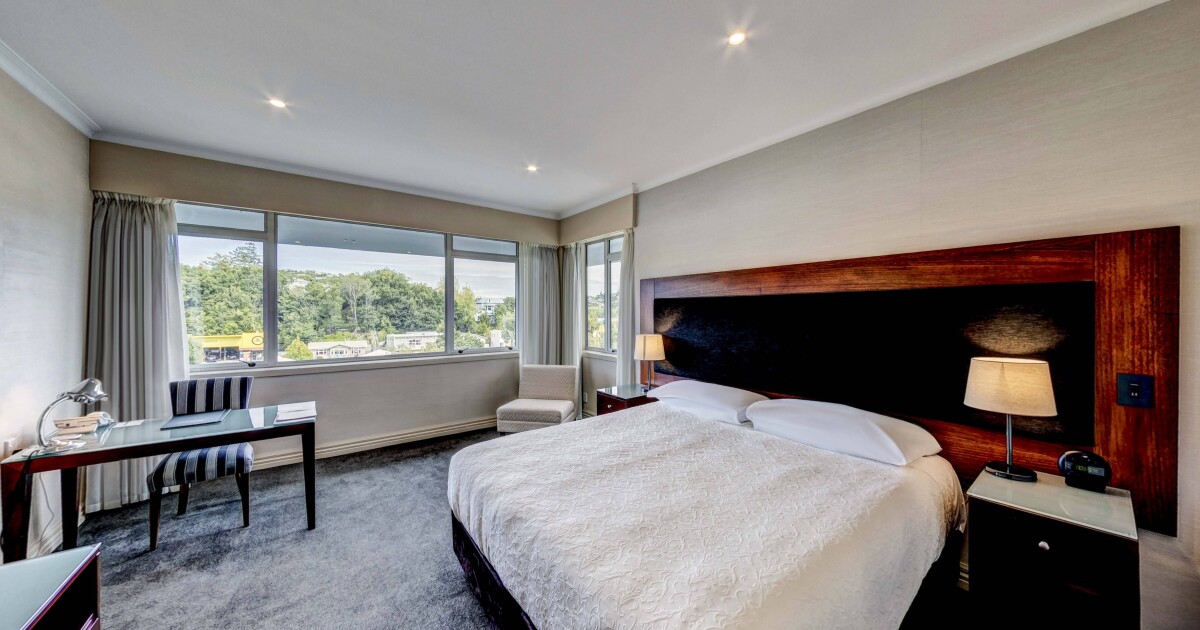 Hotel room with king bed, timber headboard, desk and city-view windows