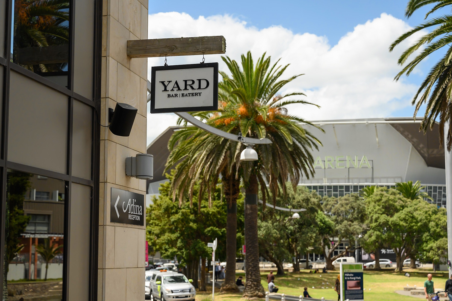 Stone-clad building exterior with hanging signage, trees and arena beyond