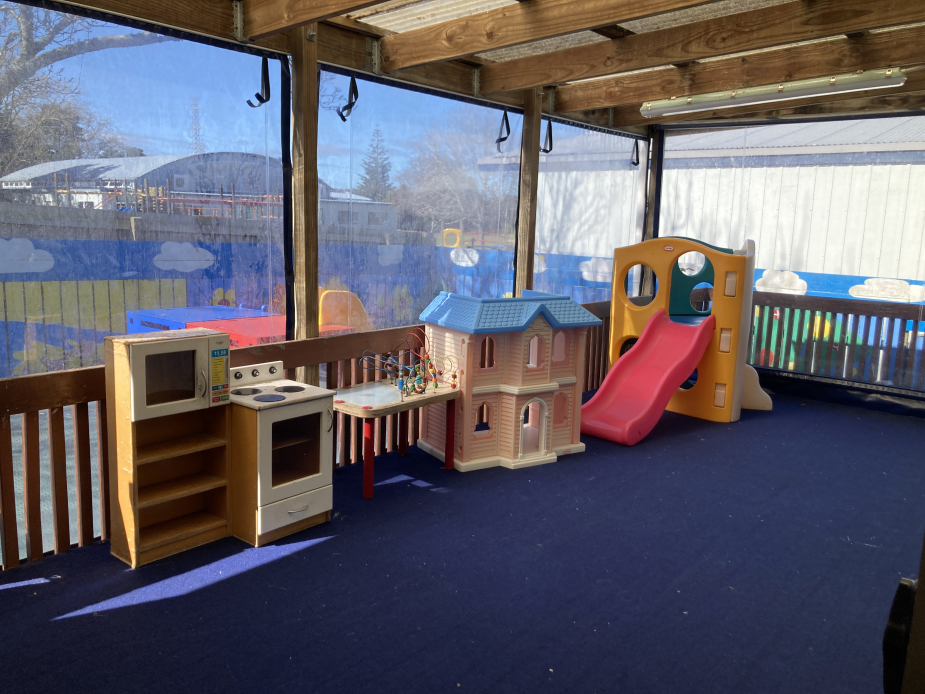Covered outdoor play area with children's play equipment and blue flooring