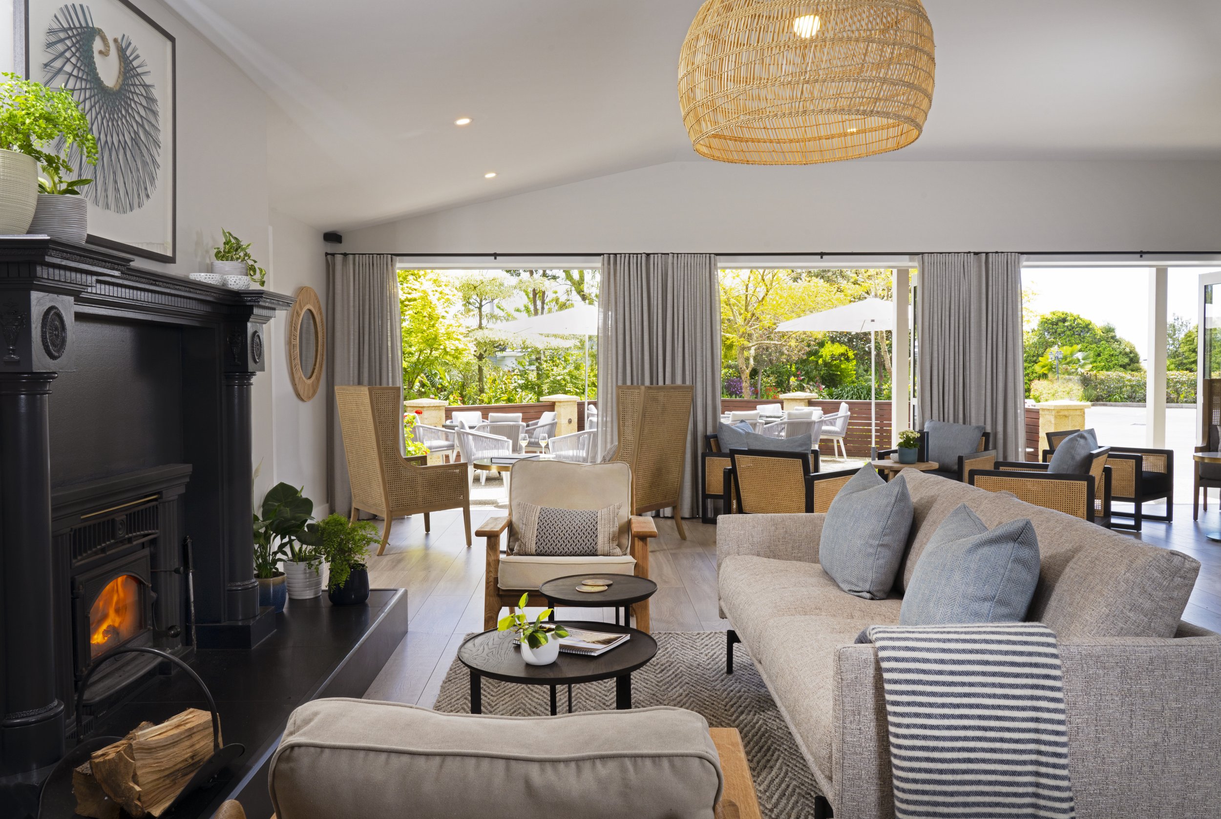 Light-filled lounge with fireplace, upholstered sofas, woven pendant, and open bifold doors to outdoor seating