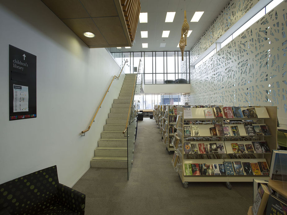 Modern library interior with decorative screen wall, staircase, and bookshelves