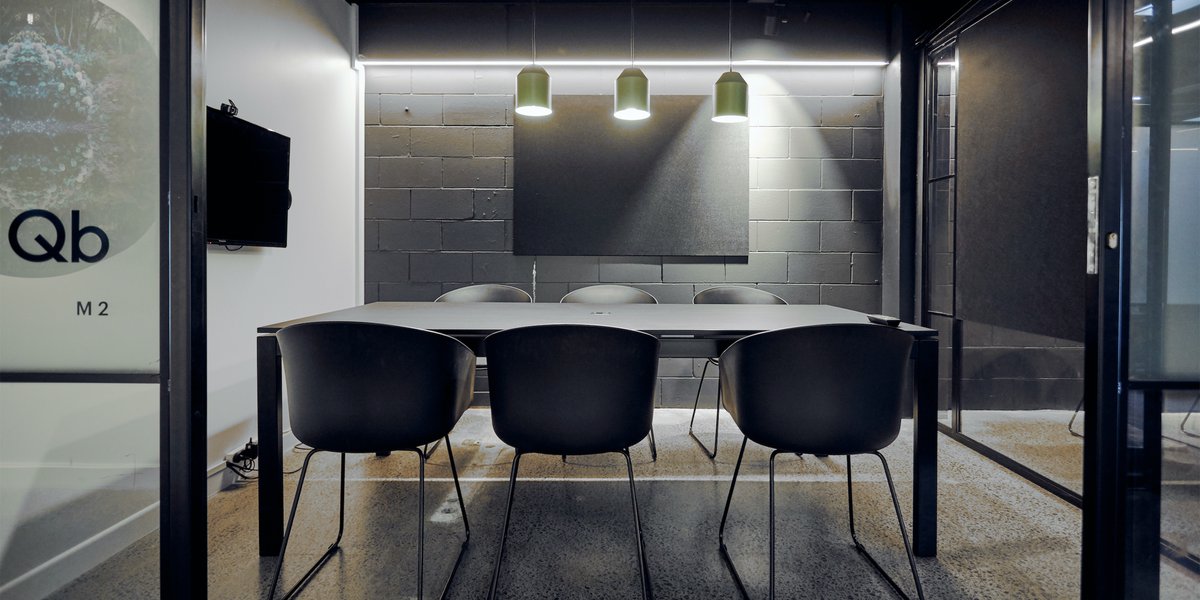 Dark meeting room with concrete block wall, black table, black chairs and green pendant lights