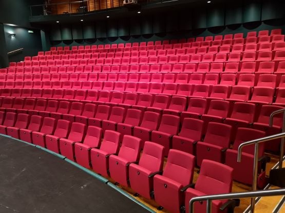 Theatre auditorium with tiered rows of red upholstered seats