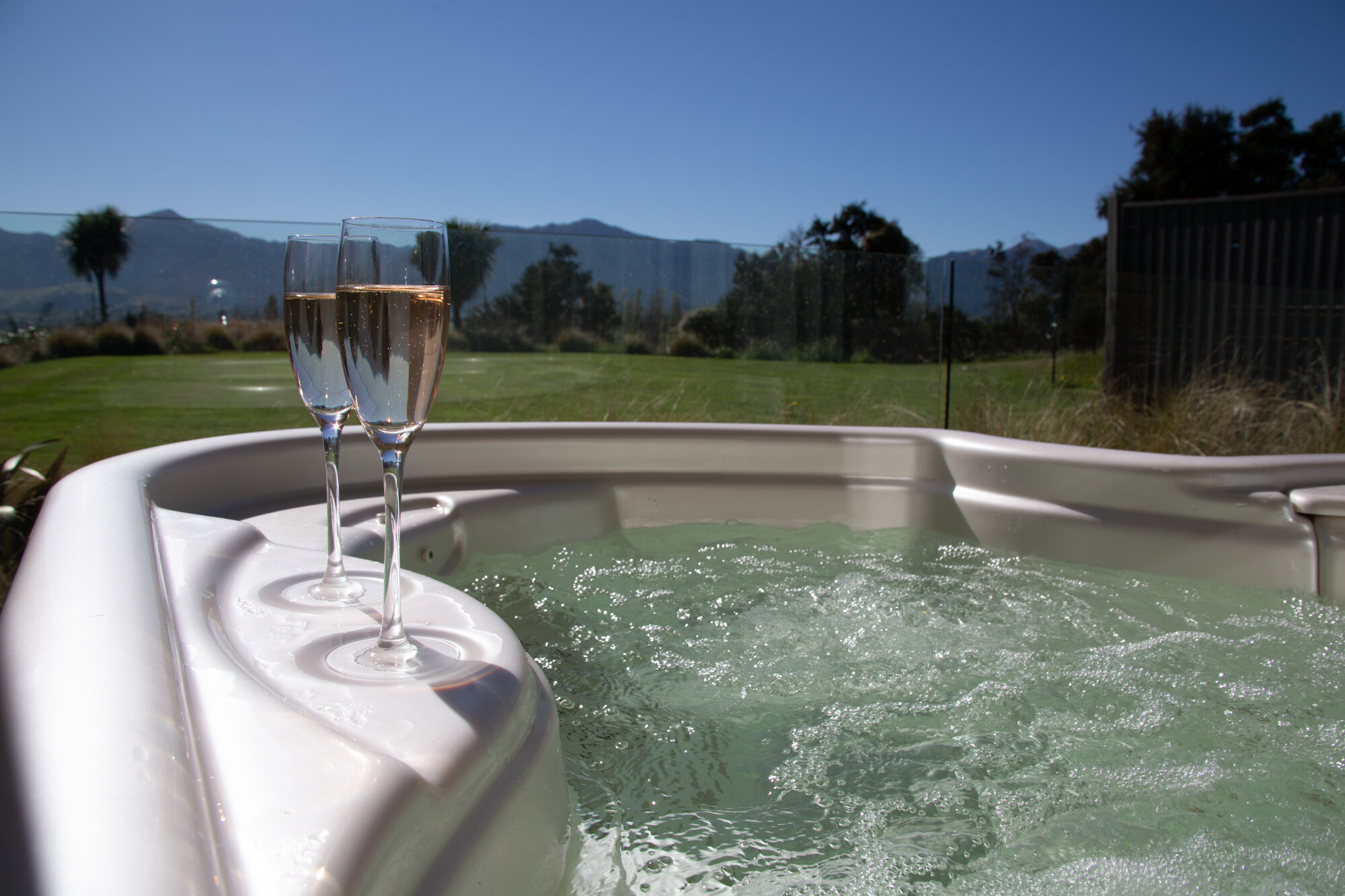 Outdoor spa pool with two champagne glasses on the edge and mountain views