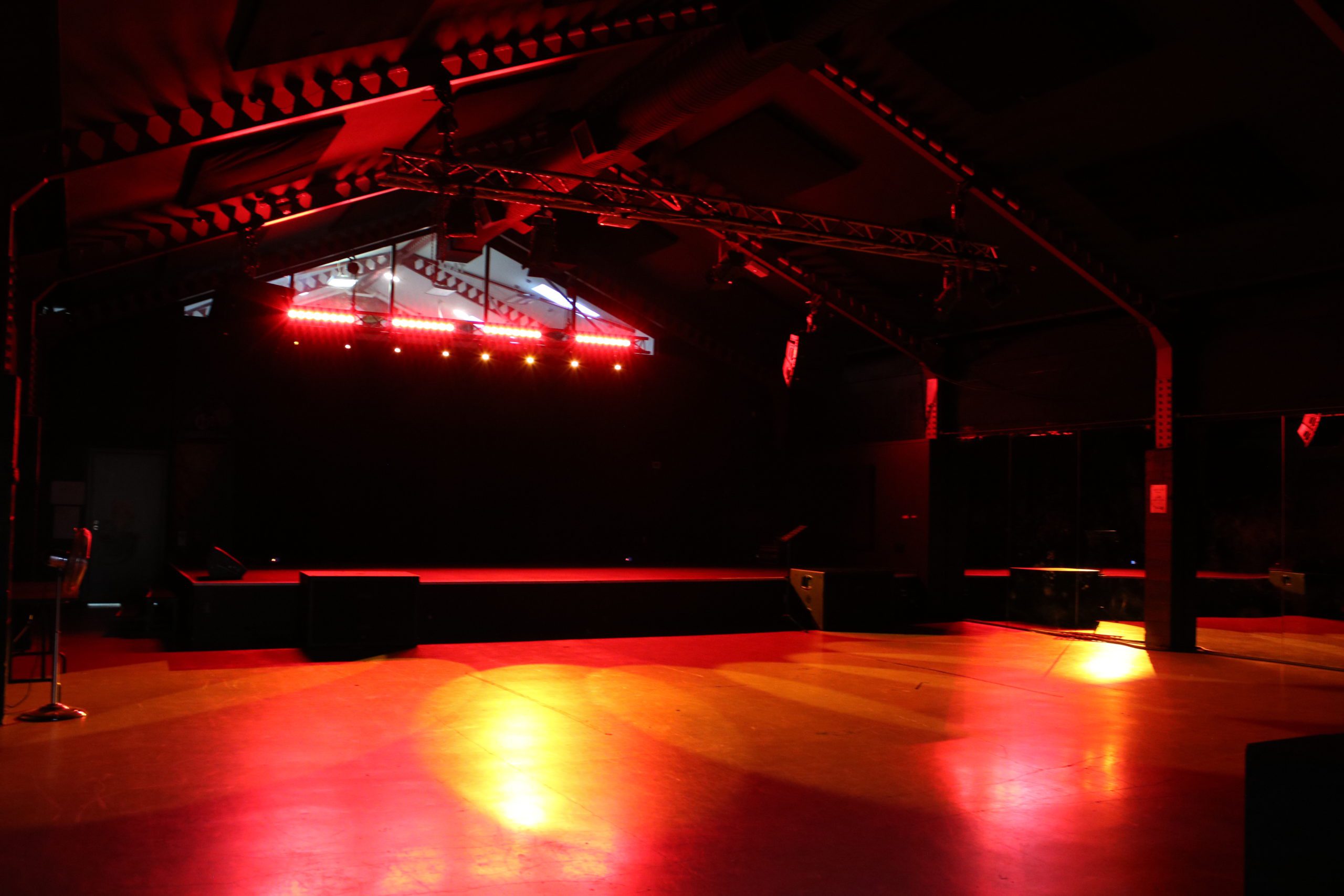 Dark warehouse interior with red stage lighting, exposed truss and open concrete floor