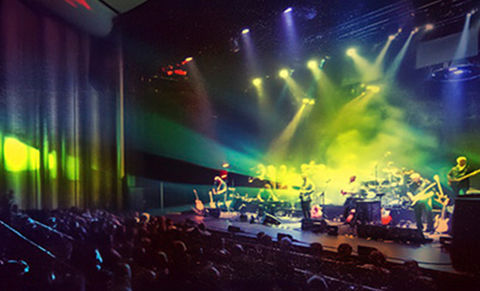 Large theatre auditorium with stage lit in coloured lights and audience seating
