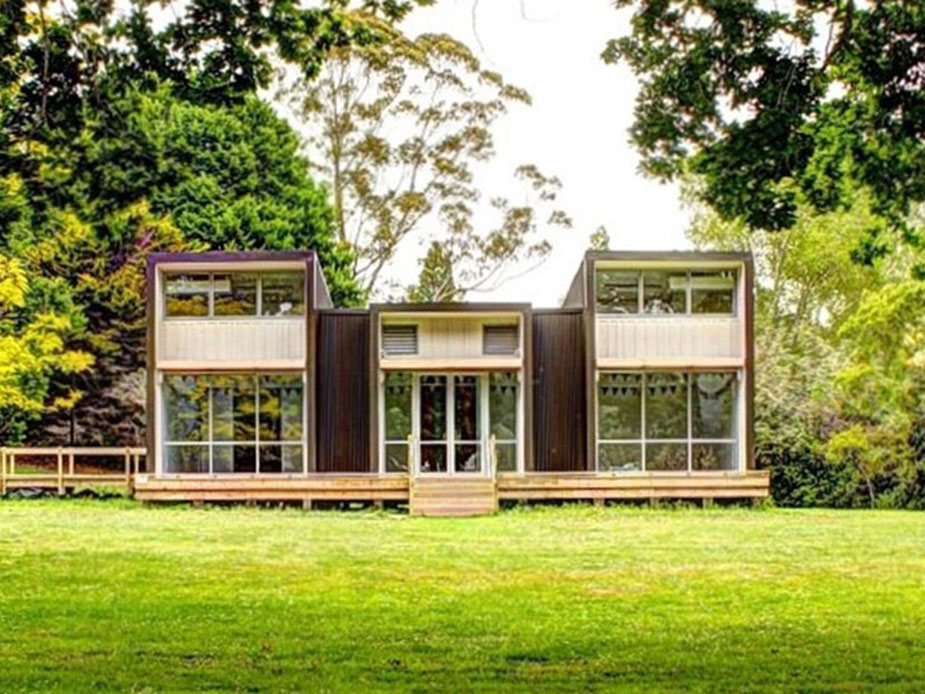Two-storey dark-clad building with extensive glazing and a timber deck, set in a grassed park
