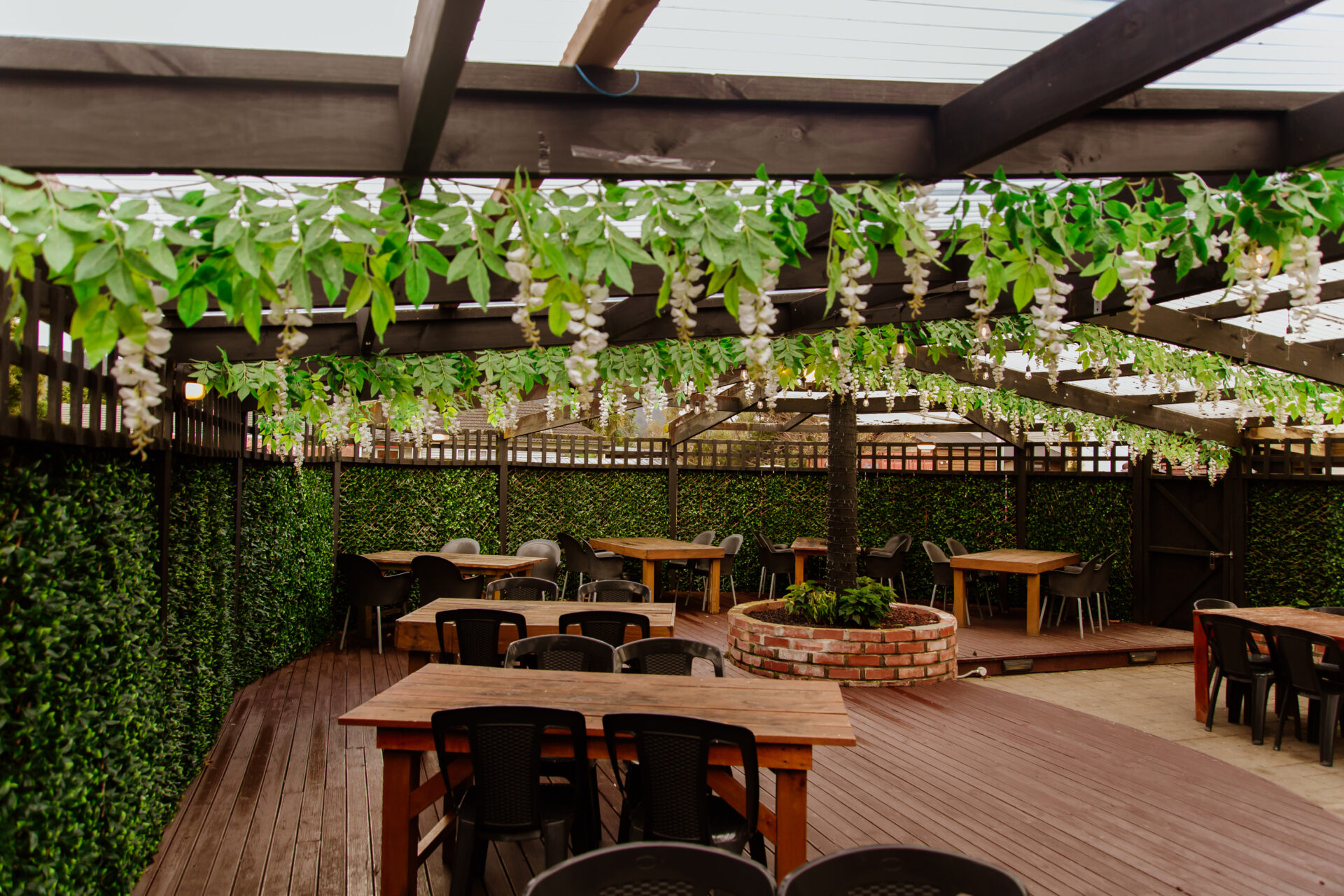 Timber deck with pergola, hanging foliage, and long dining tables