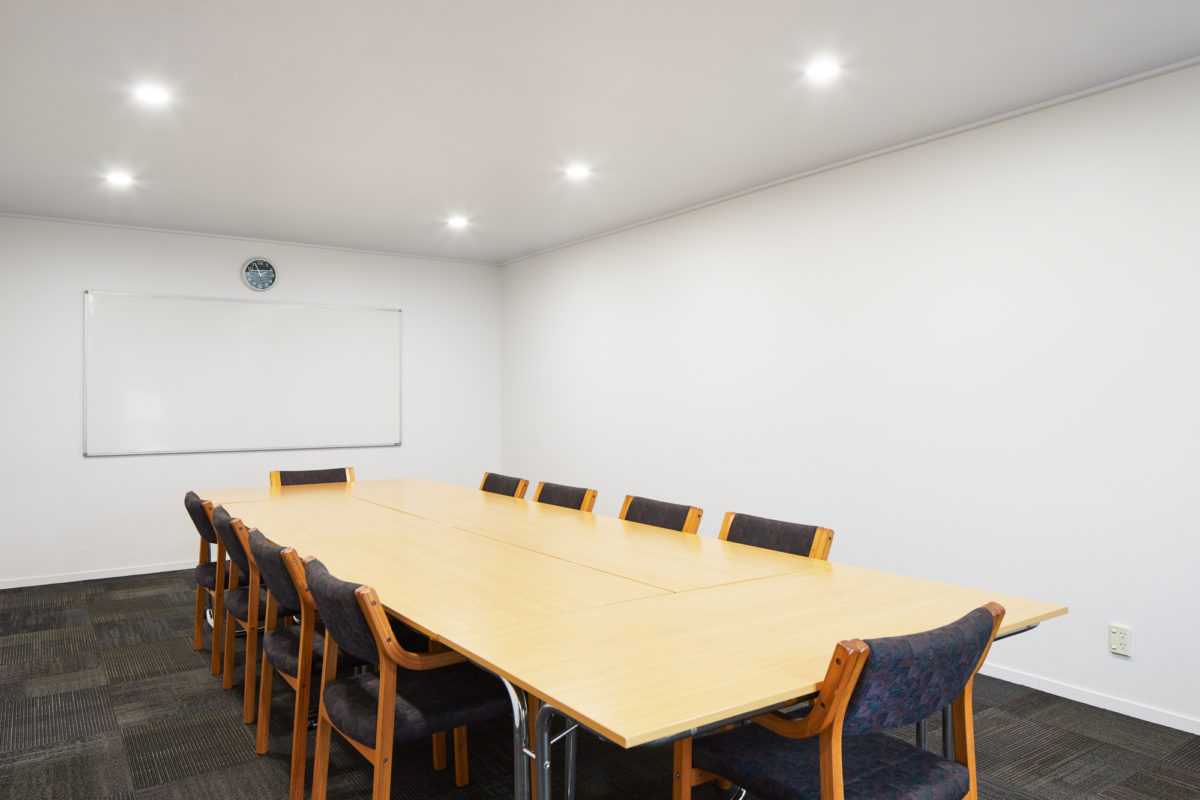 Plain meeting room with long timber table, upholstered chairs, whiteboard, recessed lighting