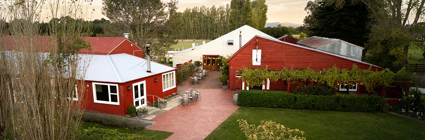 Elevated view of red timber buildings with courtyard seating and surrounding vineyard rows