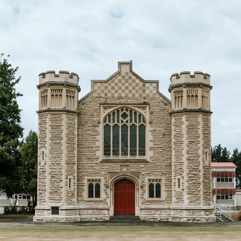Stone Gothic building with corner turrets, arched windows, and red double doors