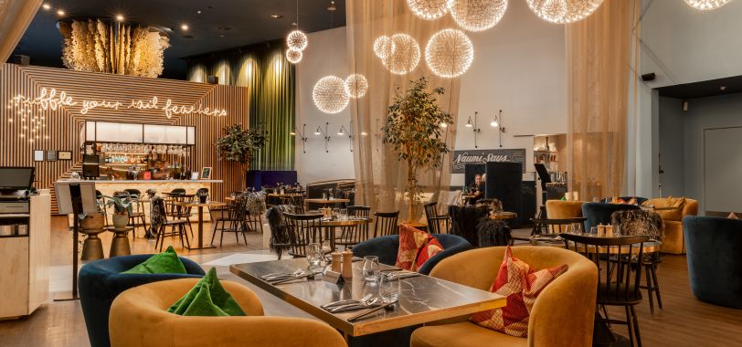 Contemporary hotel bar and restaurant with spherical pendant lights, timber slat screens, and coloured seating