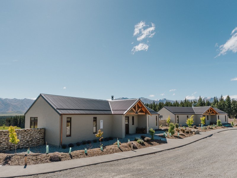 Cream render cottages with dark metal roofs and timber porch gables, mountain range behind