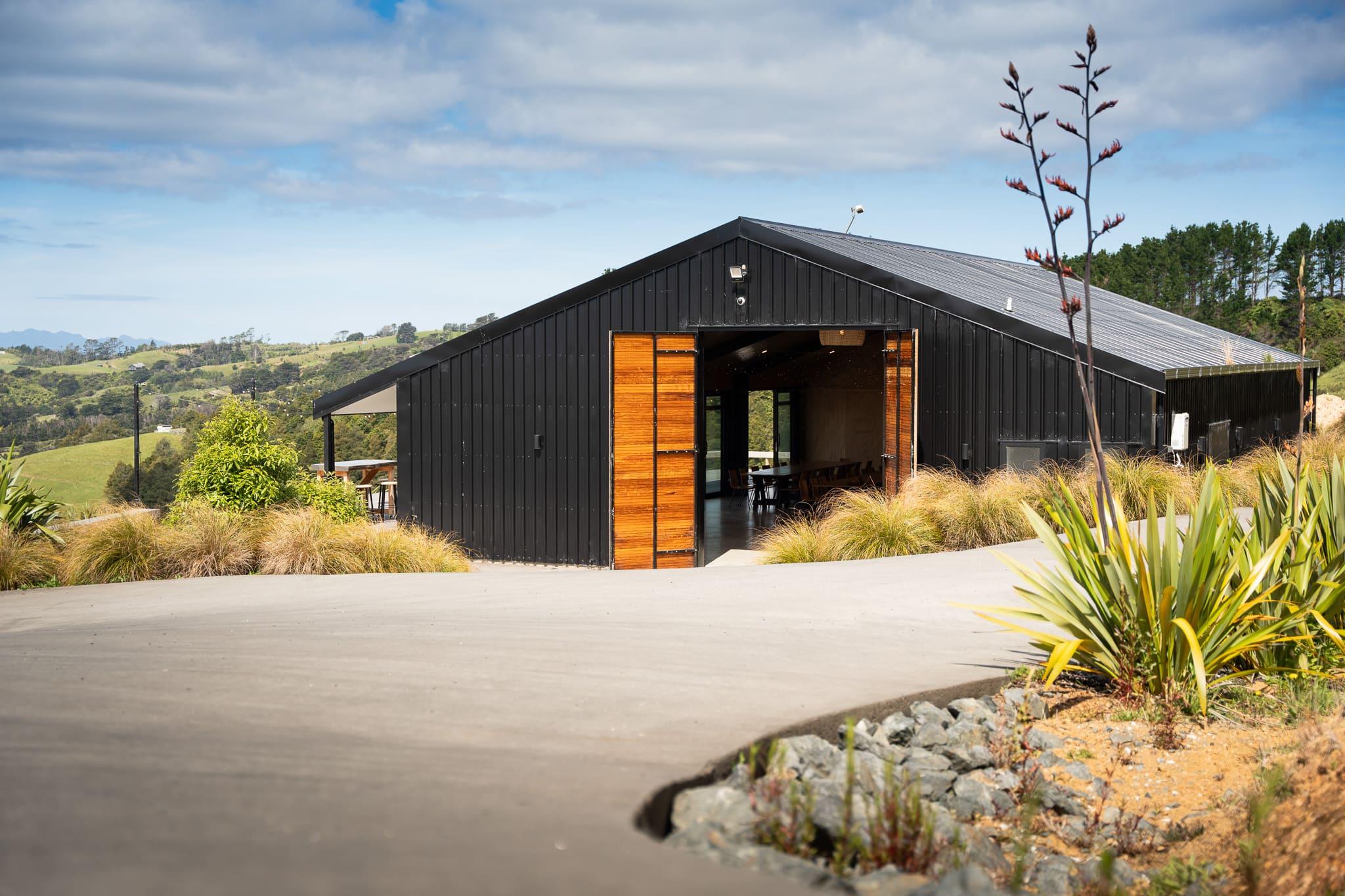Black board-and-batten barn with timber doors and native planting on a hillside farm